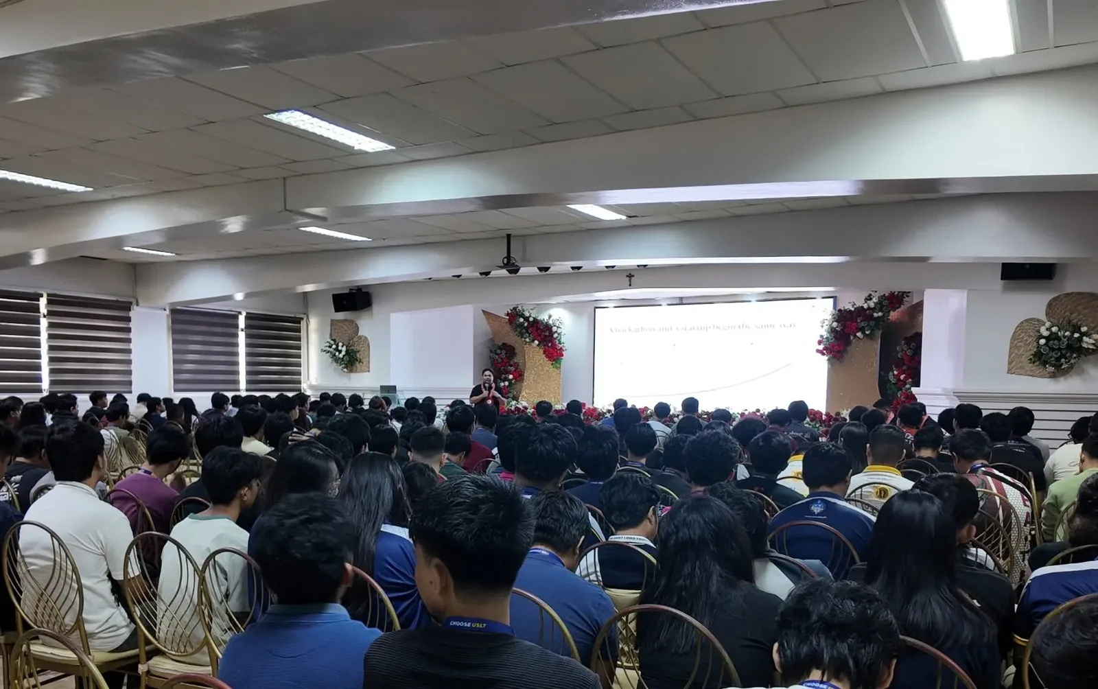 The slide "A hackathon and a startup begin the same way" on screen before a full hall of students at ITE Day 2026.